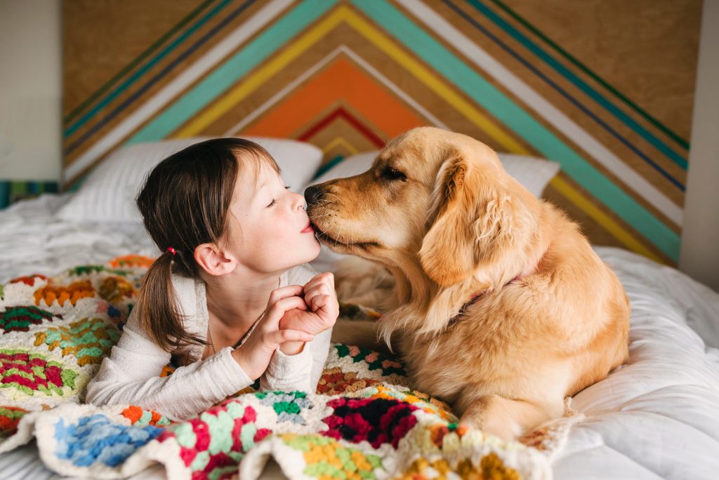 Girl lying on a bed kissing her golden retriever dog