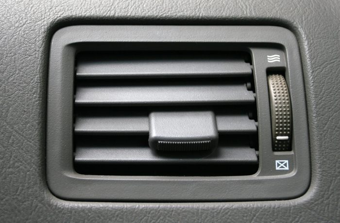 Air vent with adjustable slats and dial, embedded in a textured vehicle dashboard, for airflow control.