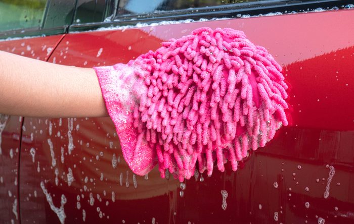 A pink glove cleans a wet, soapy red car door outdoors.
