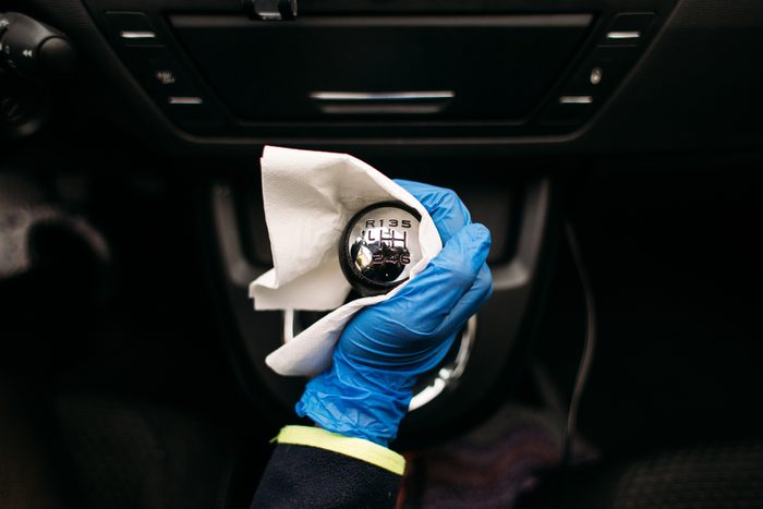 Gloved hand wipes gearshift knob inside a car. Knob displays gear pattern: R, 1-6.