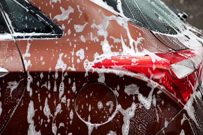 Car covered in soap suds during a wash, with visible red taillight and fuel cap on glossy brown body.