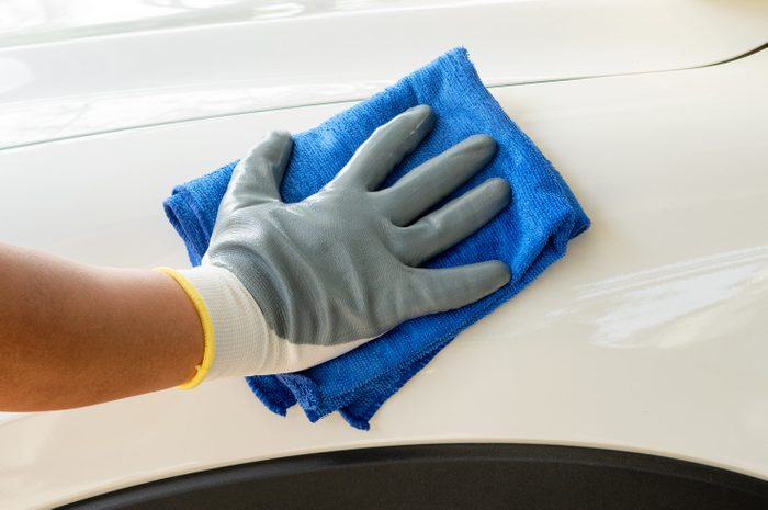 Gloved hand wipes a car's white surface with a blue cloth, highlighting cleaning action in a maintenance context.