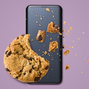 A bitten chocolate chip cookie crumbles on a smartphone screen against a purple background.