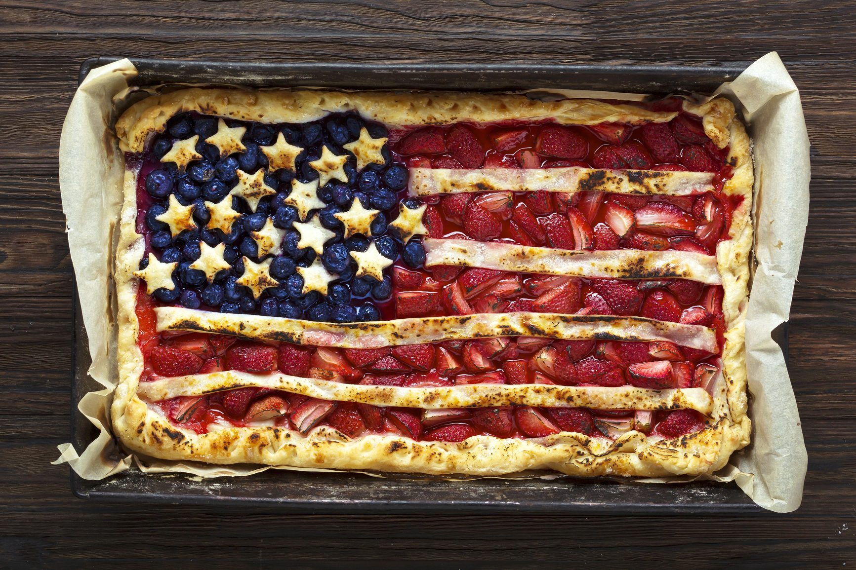 overhead view of a fruit tart designed like the american flag in a rectangular pan on a dark wood countertop