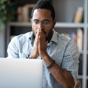 A man focuses intently on a laptop screen, seated in a room with bookshelves and plants.