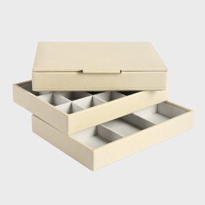 A beige jewelry organizer features stacked trays with compartments, arranged on a plain white background.