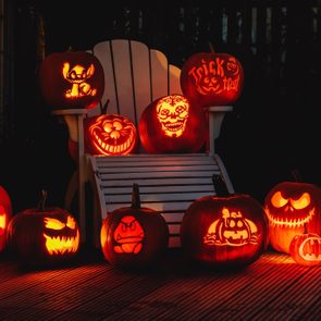 Carved pumpkins glow, illuminating Halloween designs on a white chair at night. One pumpkin has 