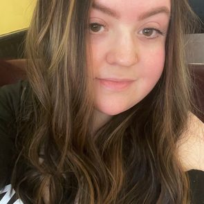 Person smiles gently, framed by long, wavy hair, indoors against a softly lit background.