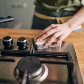 Hand uses sponge to clean a stovetop in a kitchen.