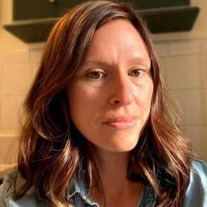 Person gazes softly, head slightly turned, with brown hair in a softly lit indoor setting featuring tiled walls.