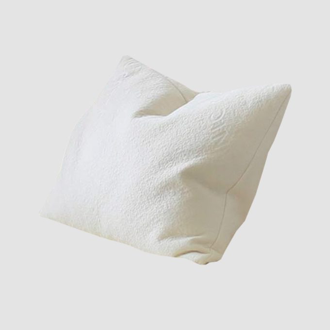 White pillow resting, slightly elevated, in a simple, light gray background.
