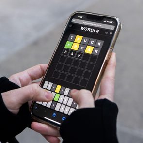 Hands hold a smartphone displaying a Wordle game with words 