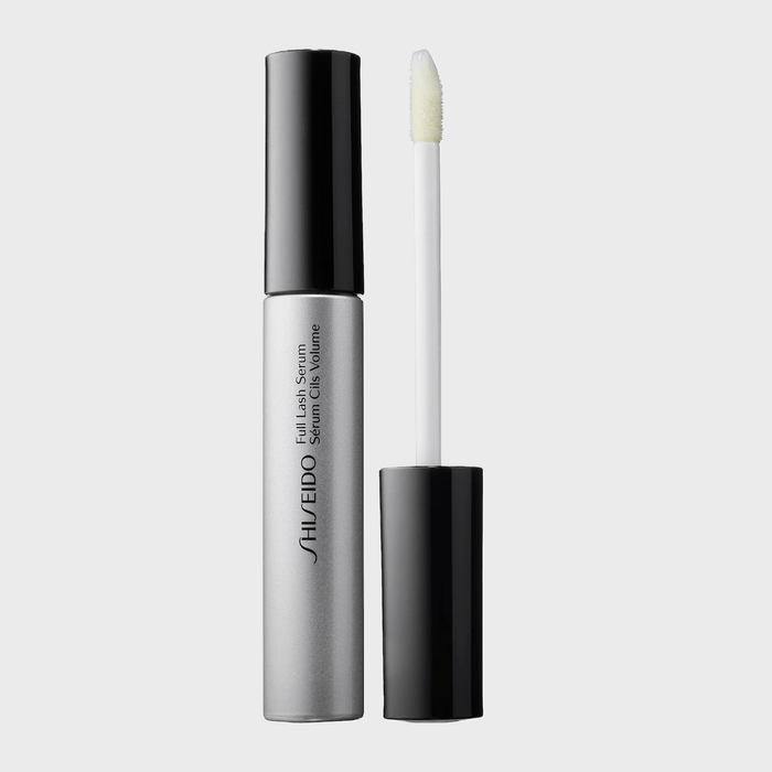 Tube of lash serum stands open, revealing a white applicator wand; sleek silver and black design, placed on a plain gray background.