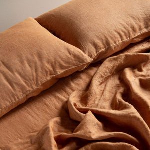 Orange pillows and crumpled sheets lie on a bed, creating a warm, cozy setting.