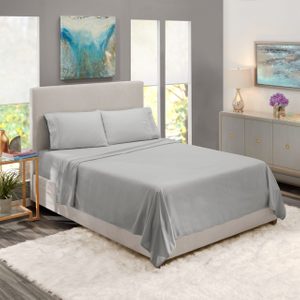 A neatly made bed with gray sheets is placed in a modern, well-lit bedroom featuring abstract artwork and minimalist furniture.