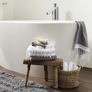 Towels rest on a wooden stool beside a bathtub, with a brush on top, set in a minimalist bathroom.