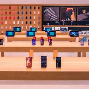 Smartphones displayed on wooden tables in a modern store; colorful phone cases are organized on the wall in the background.
