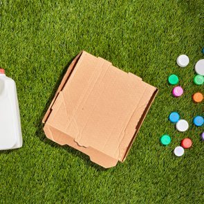 A milk jug, a cardboard box, and colorful bottle caps are placed on green grass.