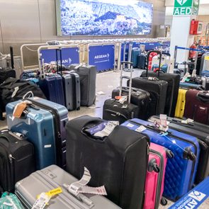 Suitcases sit unattended in an airport area, surrounded by barriers and signage displaying 
