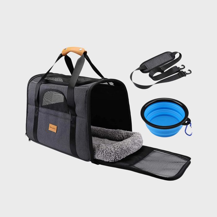 Pet carrier open with cozy interior bedding alongside a detachable shoulder strap and collapsible blue bowl on a plain background.