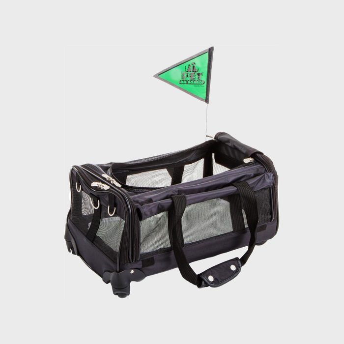 Rolling pet carrier sits on the ground, featuring mesh sides and top zippers, with a small green flag labeled 
