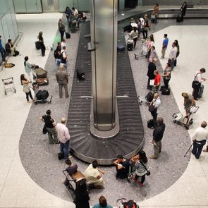 People wait around a luggage carousel, collecting baggage in a spacious airport terminal.