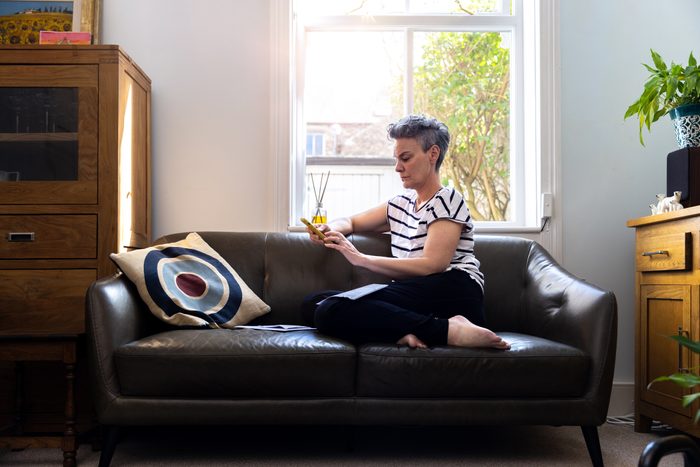 mature female adult sitting on a leather sofa. She is checking her phone with a worried and serious expression on her face.
