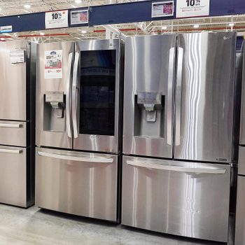 Refrigerators stand displayed in an appliance store, featuring stainless steel finishes and built-in water dispensers, promoting a sale with various discounts.