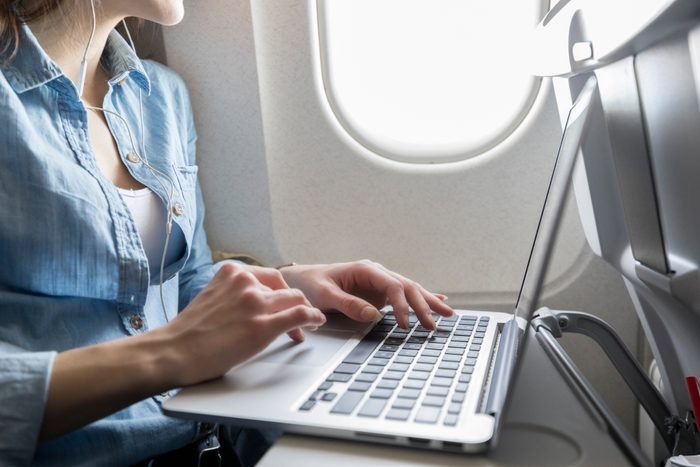 Unrecognizable young woman works while in airplane