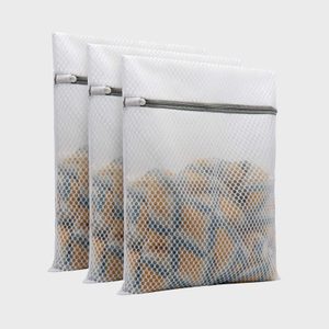 Three mesh laundry bags containing clothes, zipped closed, set against a plain background.