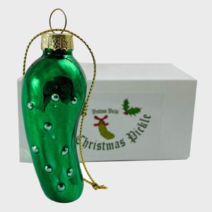 Green glass pickle ornament hangs from gold string; rests against a white box labeled 