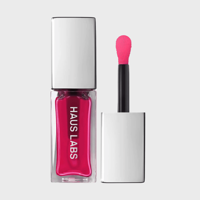 A lipstick container displays its bright pink color, with an applicator beside it, set against a plain background. Text reads 