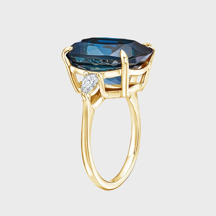 Gold ring displays a large blue gemstone in an elegant setting with small diamond accents, against a plain white background.