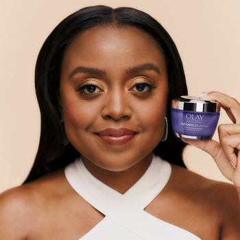 Person holding a jar of Olay Regenerist Retinol 24 + Peptide night moisturizer, smiling against a neutral background.
