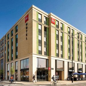 A hotel building features large windows and cyclists in an urban street under a clear blue sky.