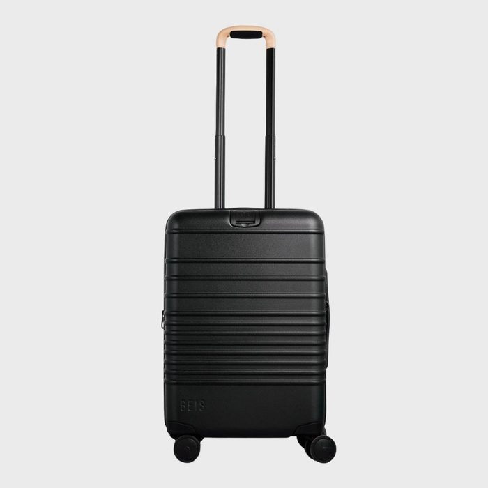 Black suitcase with a tan handle extended upward, standing on four wheels. It is set against a plain, light-gray background.