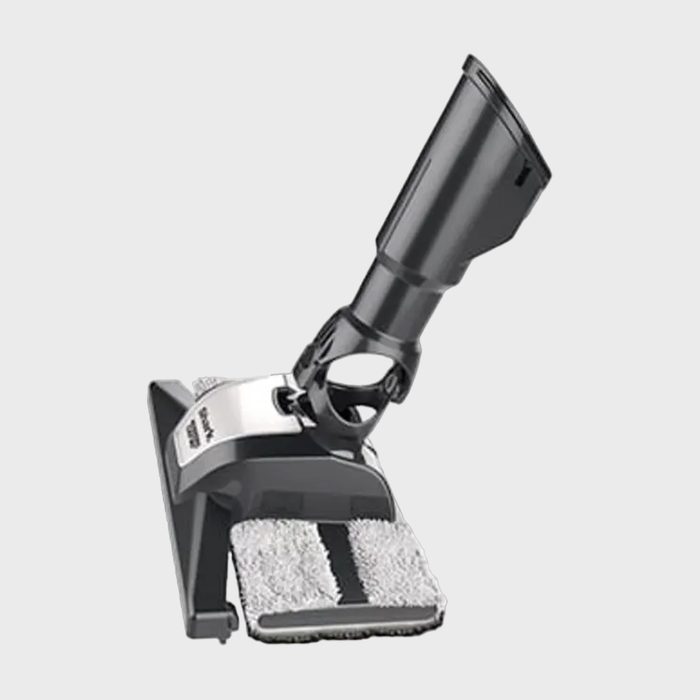 A black vacuum attachment with a cleaning pad is angled upward against a plain gray background.