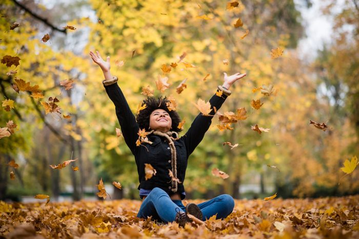 Joyous teen playing with dry maple leaves