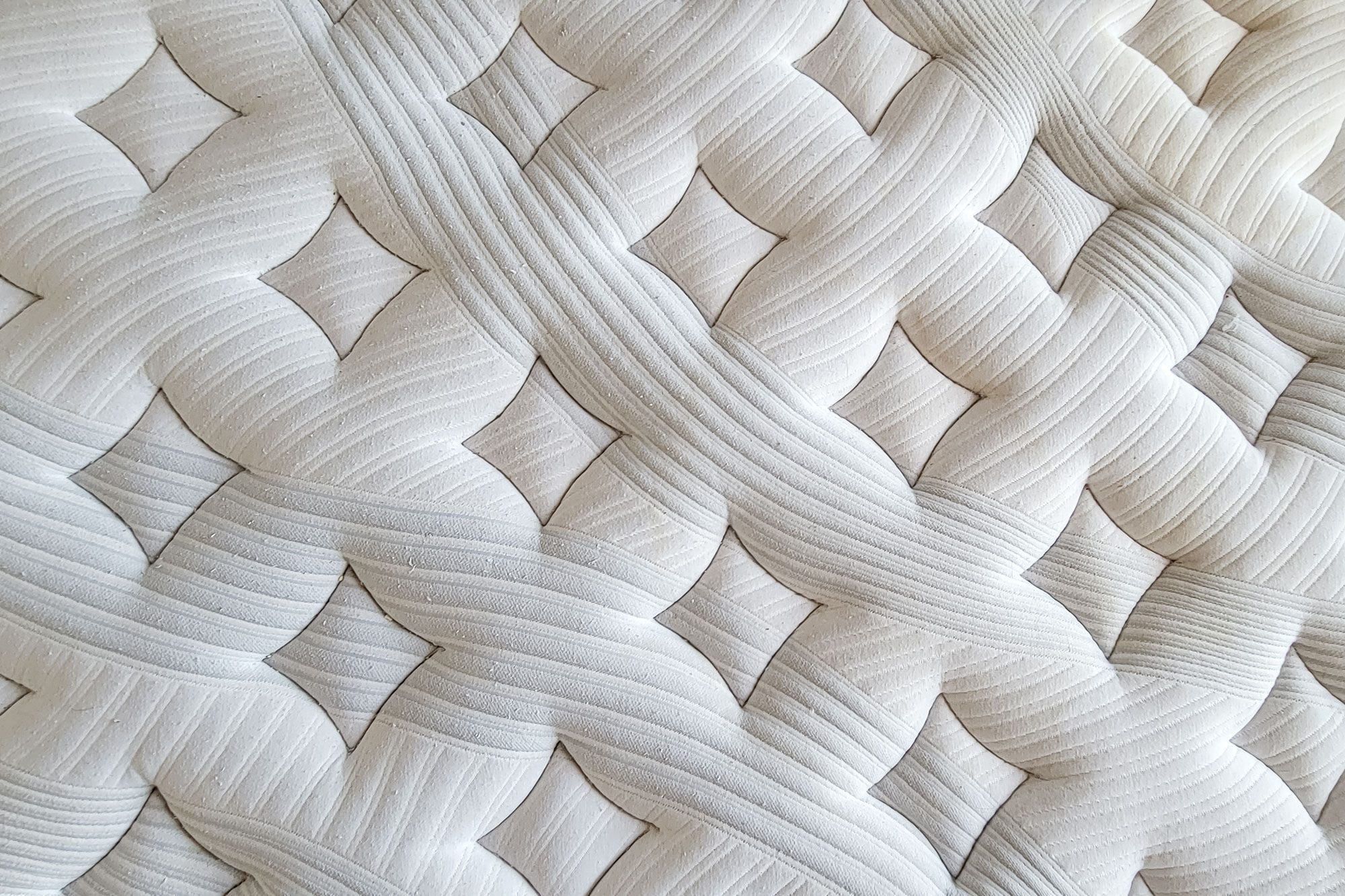 Woven white fabric displays an intricate, interlocking pattern with ribbed texture, creating an abstract, textured surface.