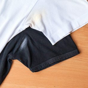 White and black T-shirts overlap, showing armpit stains on both, against a wooden surface.