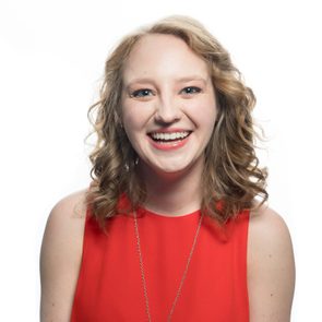 Person smiling broadly, wearing a red sleeveless top, against a plain white background.