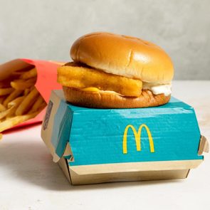 Fish sandwich sits on branded box; fries spill from red carton on a light surface background.