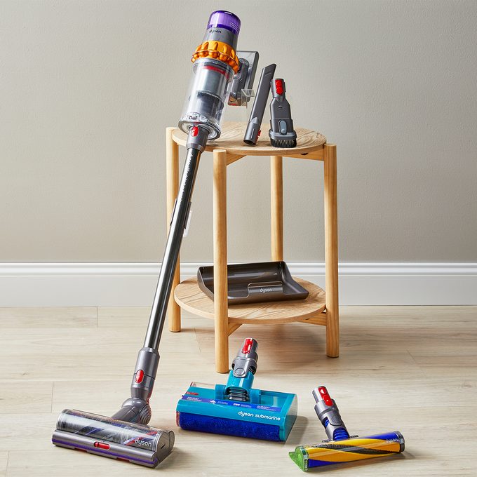 Vacuum attachments arranged neatly on the floor and a wooden table, set against a plain wall, showcasing a variety of cleaning tools.