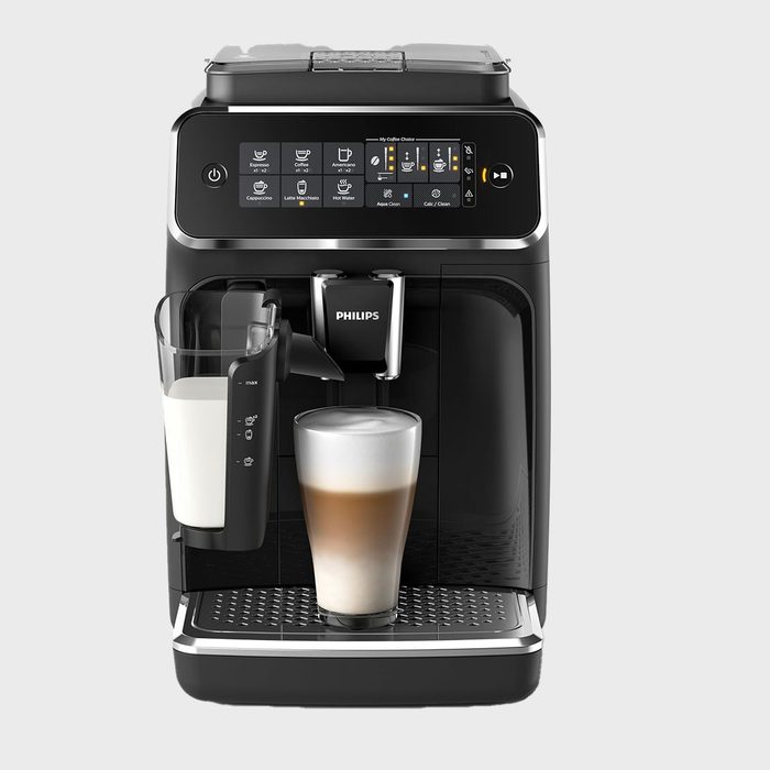 Coffee machine prepares latte macchiato; displayed on a digital interface; glass of frothed milk beneath spout; set against a neutral backdrop.