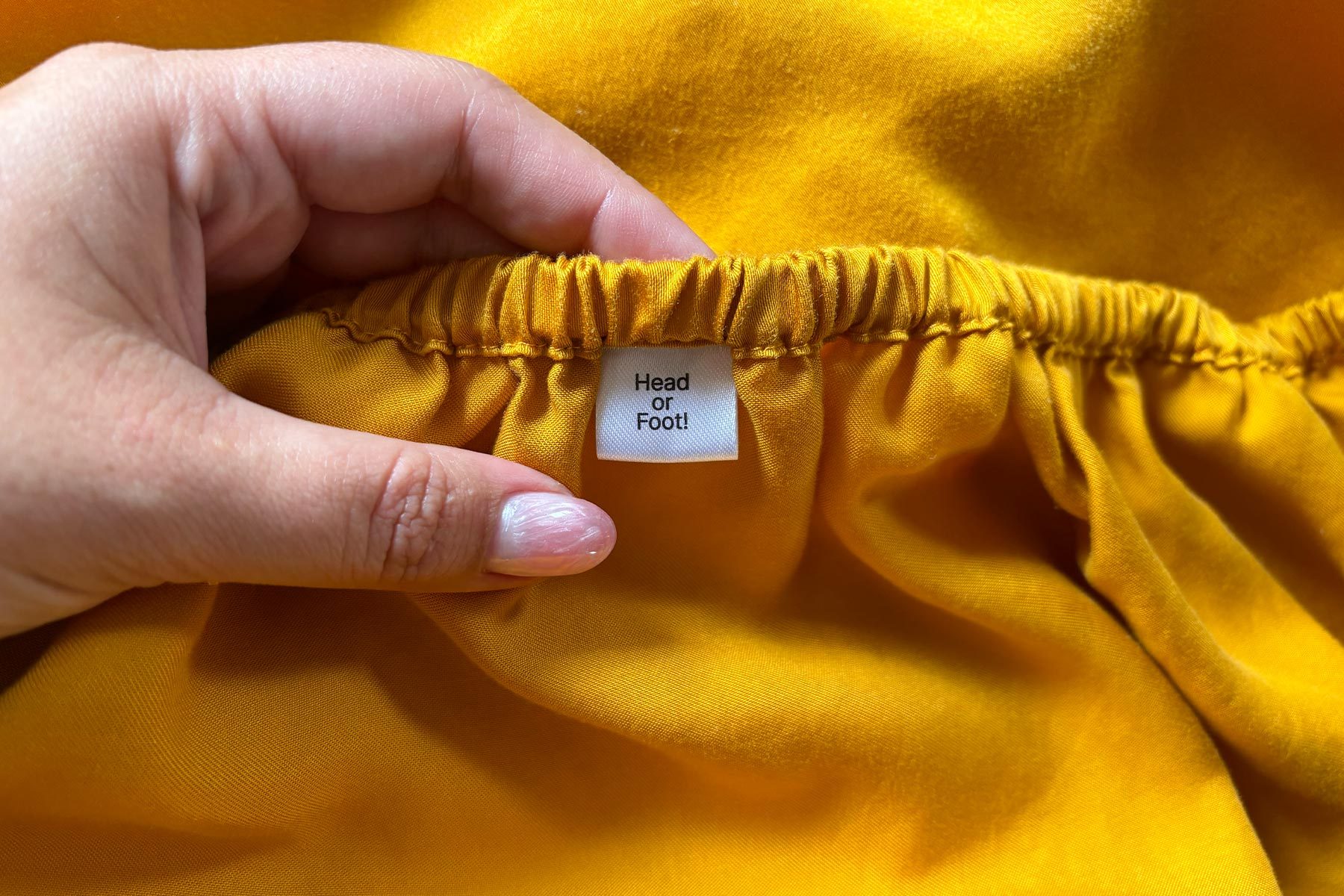 A hand holds yellow fabric with a tag reading "Head or Foot!" against a bright background.