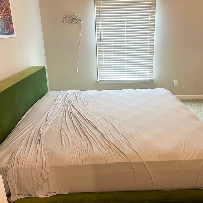 Bed with rumpled white sheet partially covering it, in a room with a 