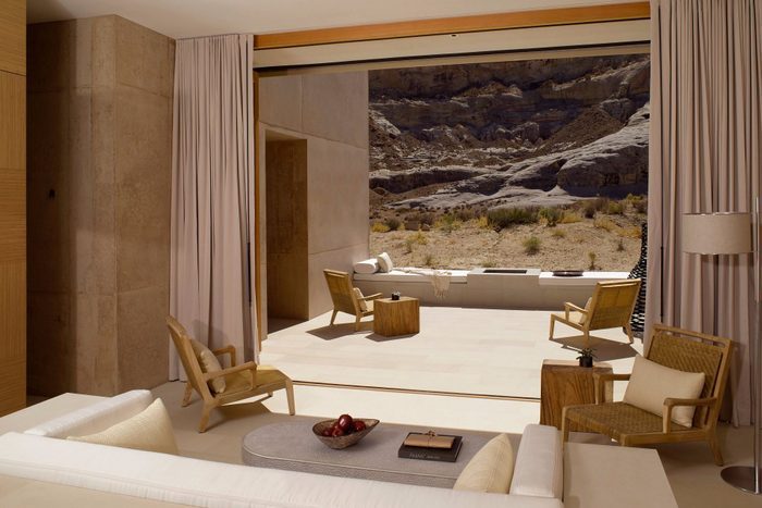 Room opens to patio, showcasing desert landscape; chairs and tables are arranged in warm, minimalist decor.