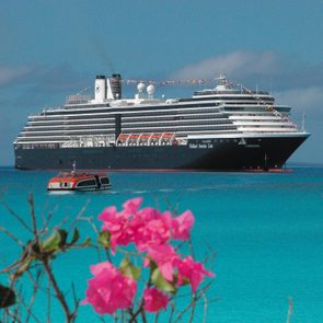 Cruise ship anchored in turquoise water, adorned with colorful flags, with pink flowers in the foreground. Text reads 
