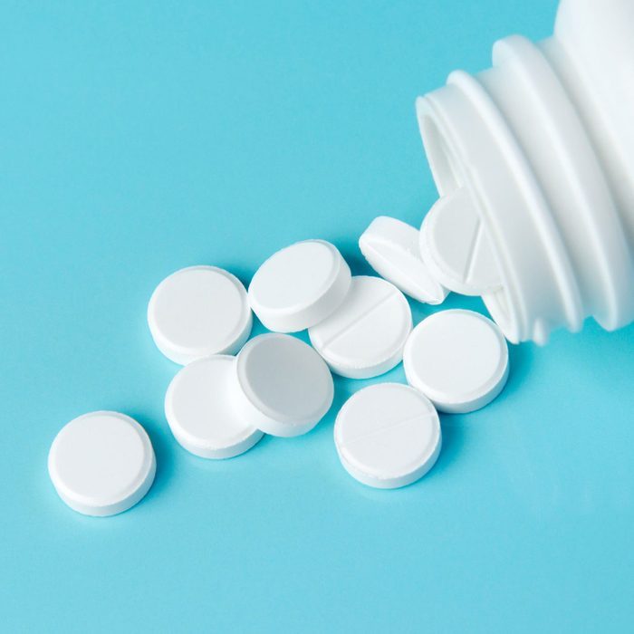 White pills spill from a bottle onto a blue background.