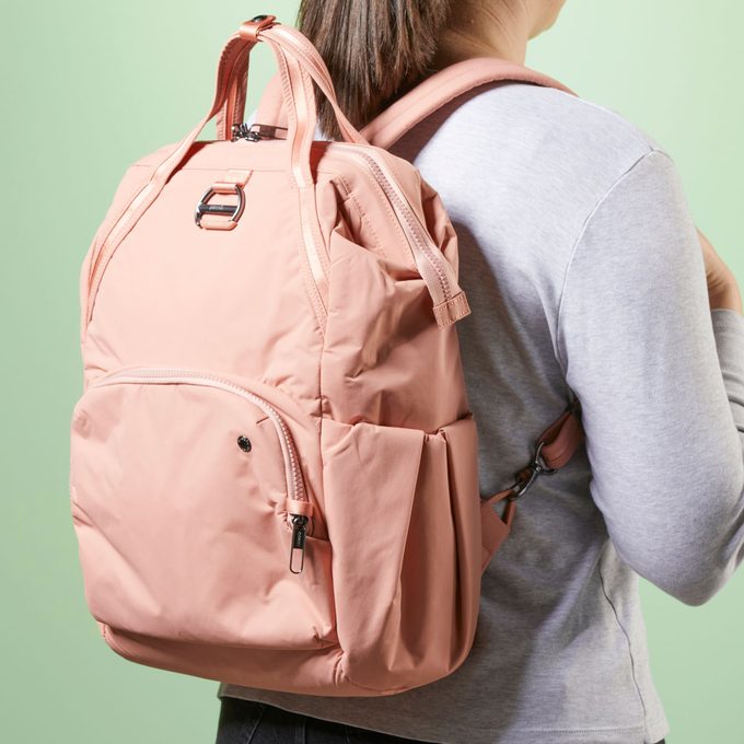 Backpack worn by a person, slightly open with visible zippers, set against a light green background.